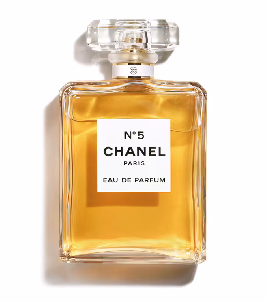 A clear glass bottle of Chanel No. 5 Eau de Parfum, with golden liquid inside and a rectangular faceted cap, shown against a white background. Marketing Made Clear A clear glass bottle of Chanel No. 5 Eau de Parfum, with golden liquid inside and a rectangular faceted cap, shown against a white background. Marketing Made Clear