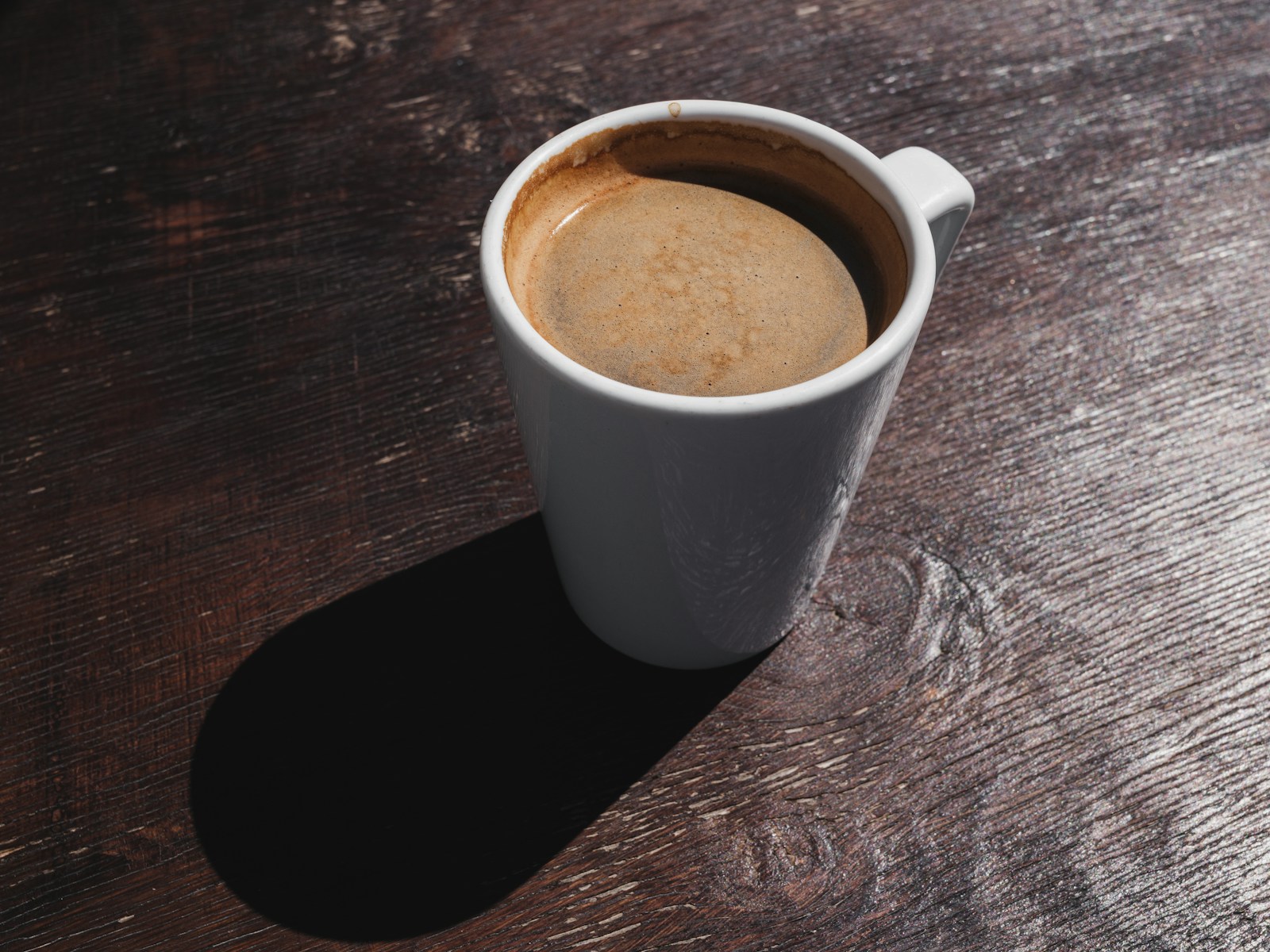 A dark Americano coffee on a table in a warmly lit coffee setting.