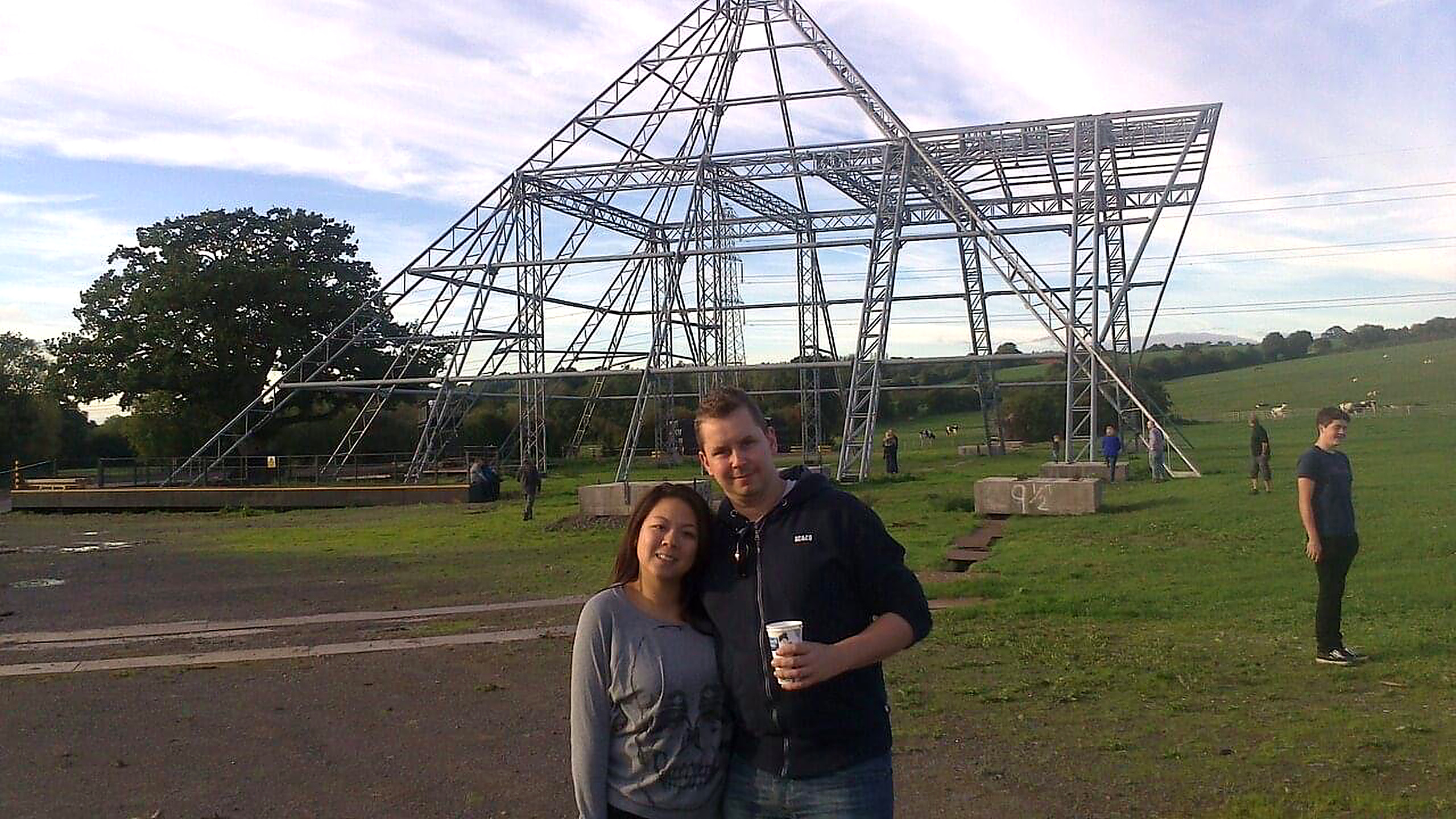 A smiling couple stands in front of a large, metal pyramid frame structure on a grassy field, with people and trees in the background under a partly cloudy sky. Marketing Made Clear A smiling couple stands in front of a large, metal pyramid frame structure on a grassy field, with people and trees in the background under a partly cloudy sky. Marketing Made Clear